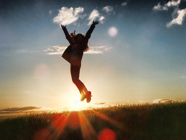 逆光の陽の光をバックに、草原でジャンプする女性。