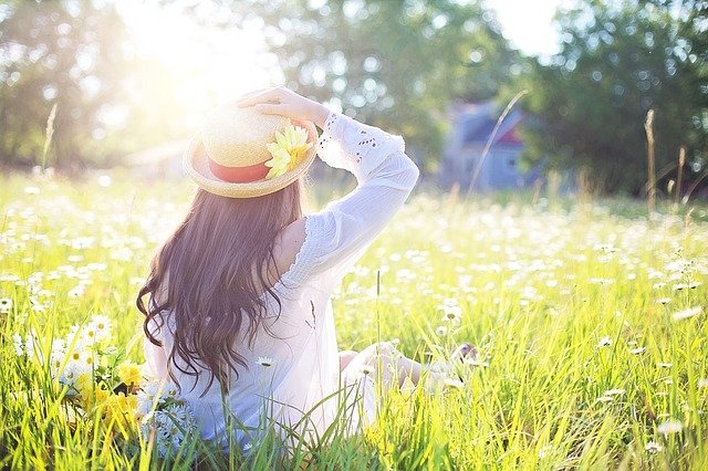 春の草原に座る麦わら帽子の少女の写真。
