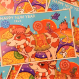 2021年丑年の、赤いホルスタイン牛とアマビエと羊の描かれた「クリエイターズ年賀状」がバラバラにたくさん並べられた写真。
