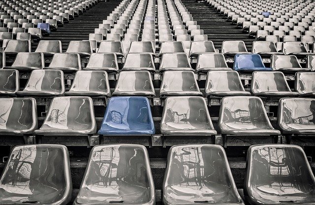 グレー＆ブルーの、艶のある座席が並ぶ無観客のスタジアム写真。