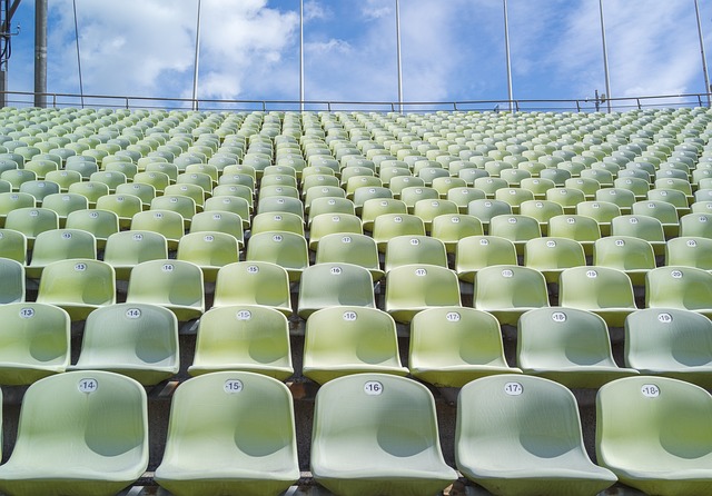 グレーがかった黄緑色の、無観客のスタンド席と、球場の外の青空と雲の写真。